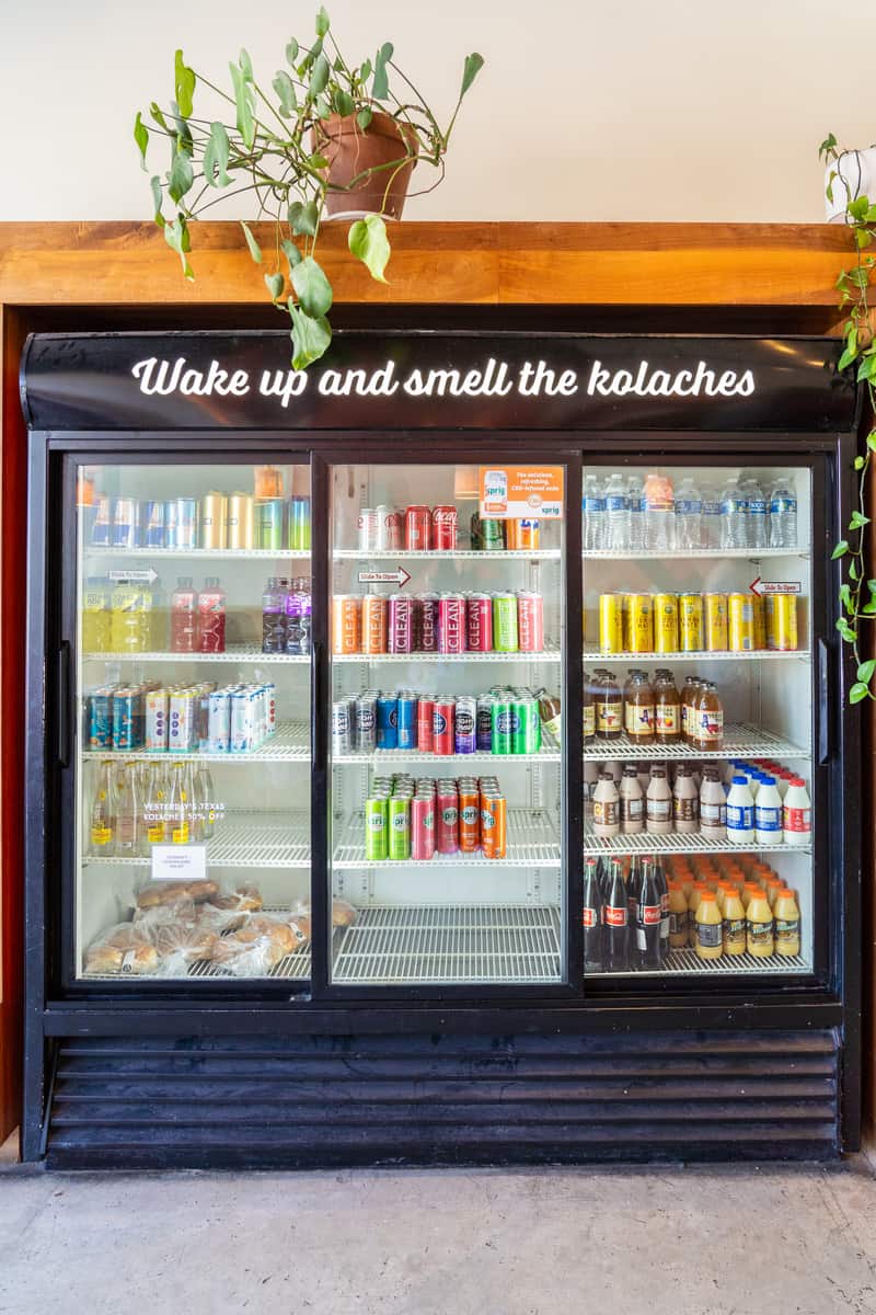Stocked beverage fridge with the words "wake up and smell the kolaches" above it