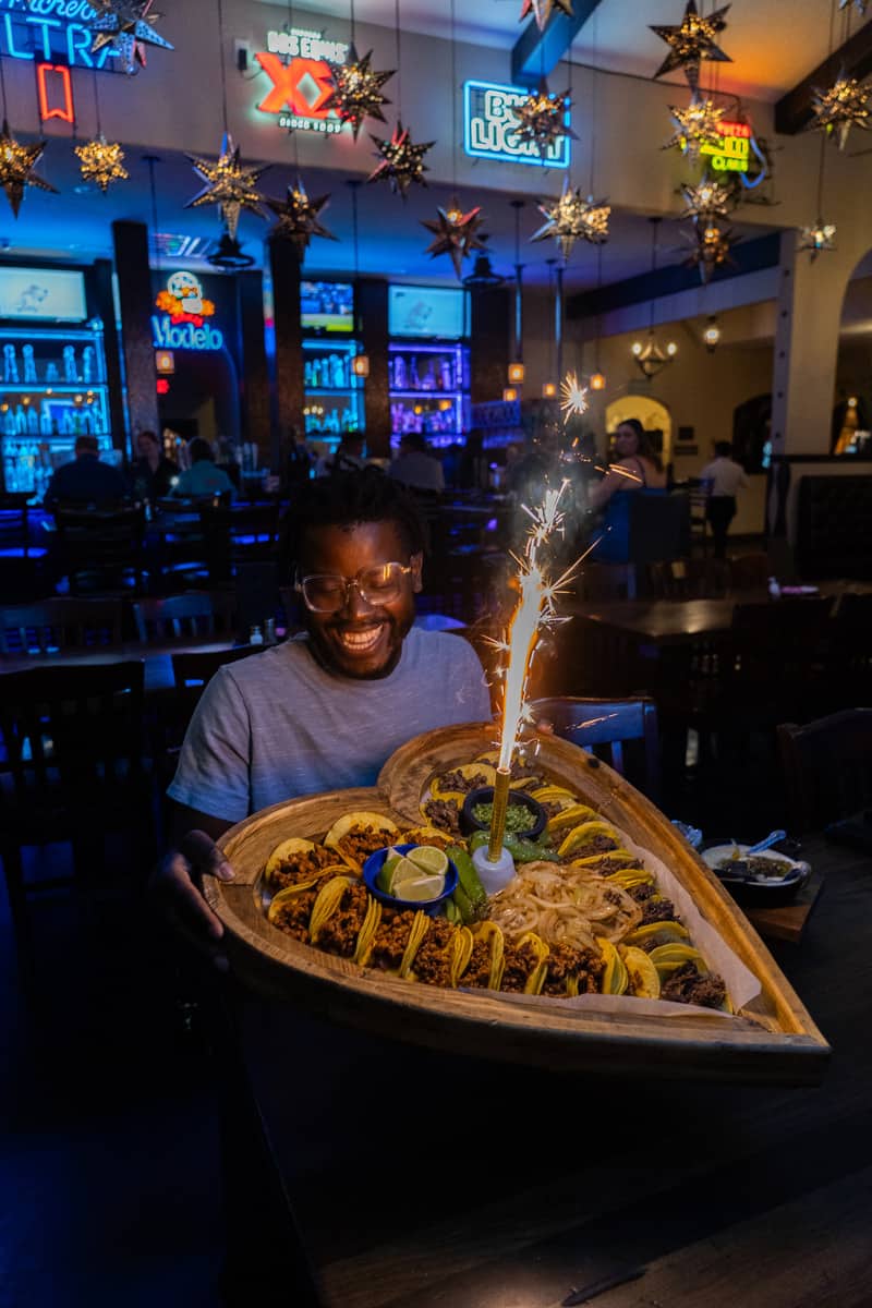Man holding a tray of 24 tacos with a sparkler in the middle