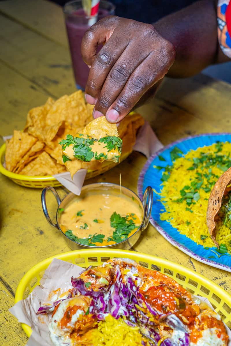 Man's hand holding a chip with Curry Queso on it