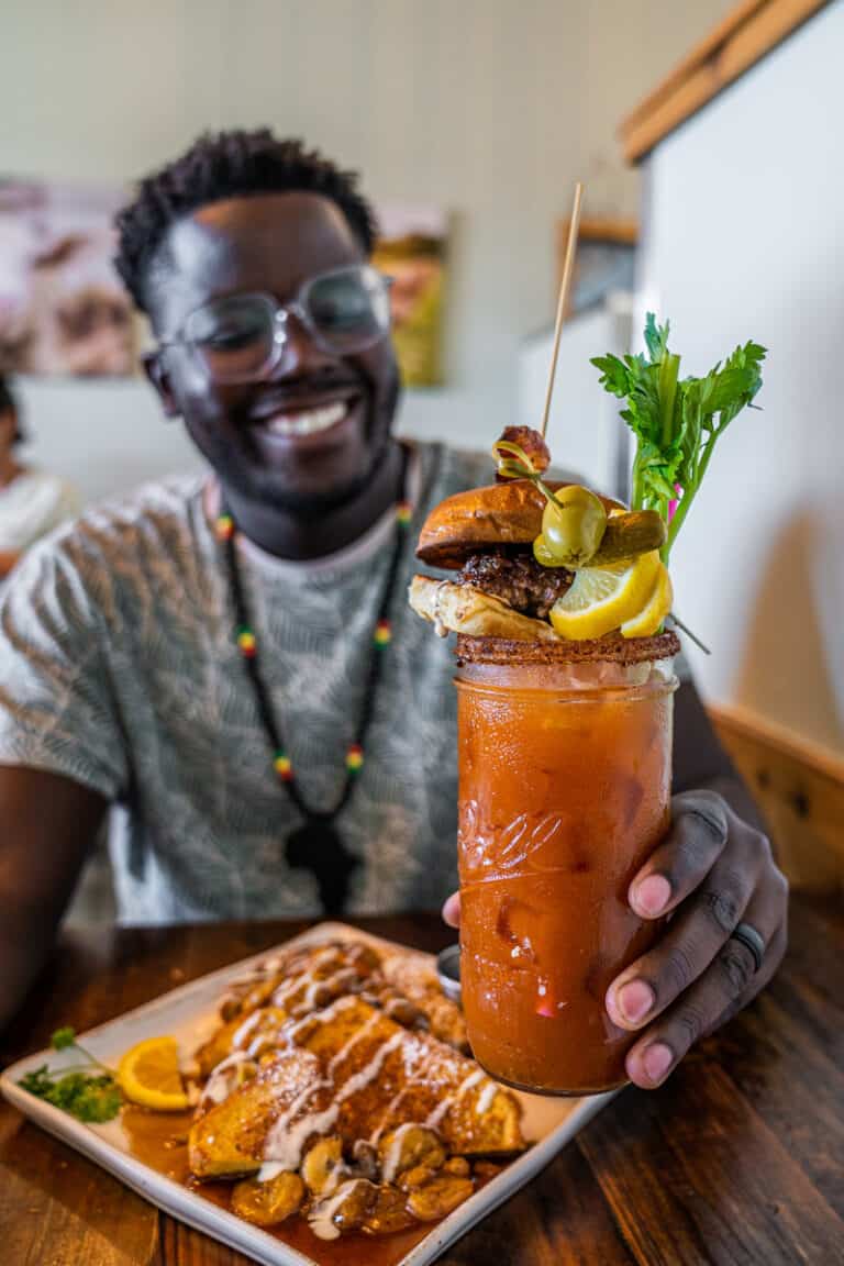 Man holding a Bloody Mary with a plate of French toast in front of him