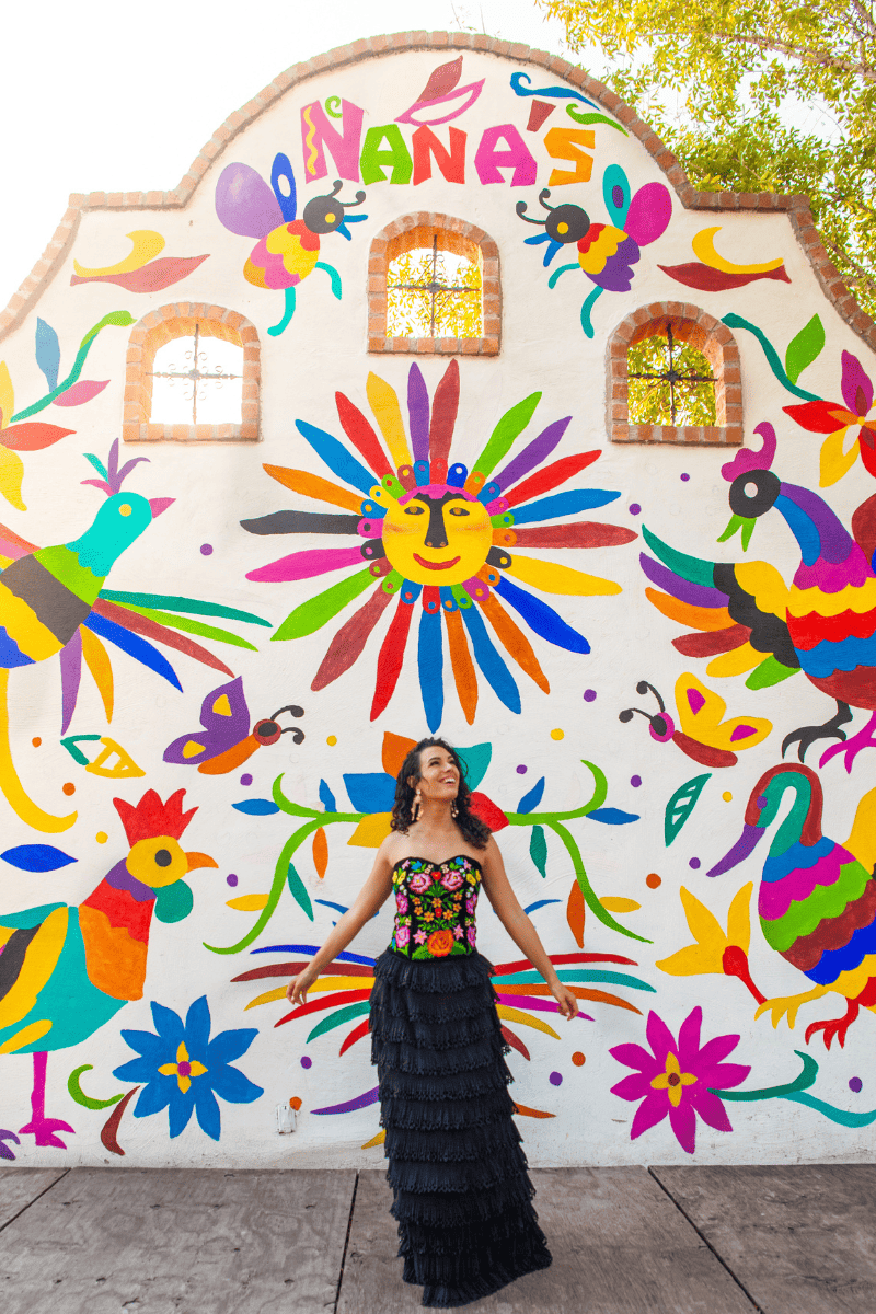 A woman posing in front of a colorful mural.


