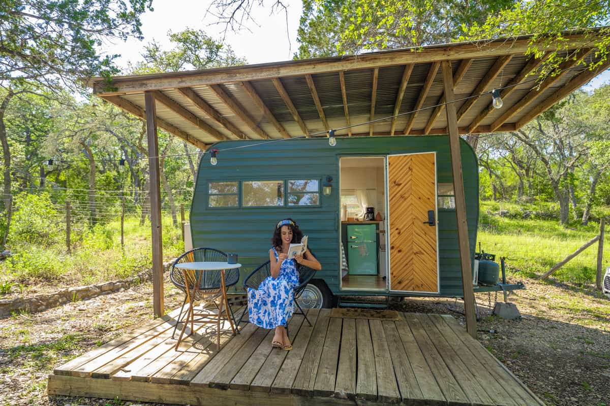 Woman sitting outside a camper on a covered patio with a book