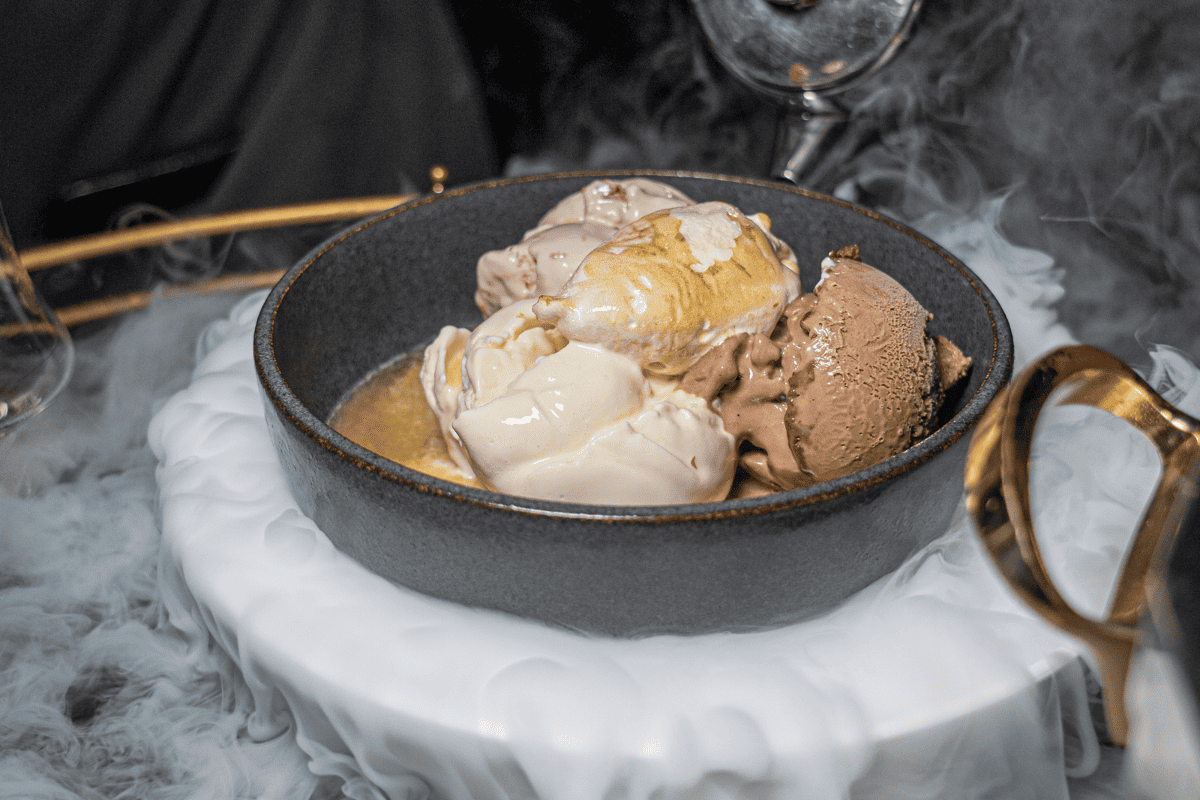 A bowl of ice cream with dry ice vapor on a plate, creating a dramatic smoky effect.