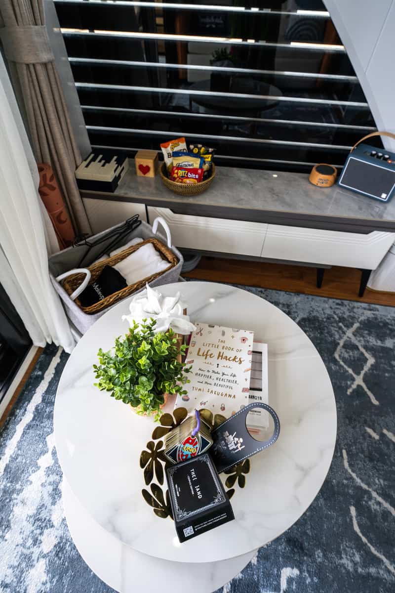 Modern room with a white marble table holding books, snacks, a plant, and personal items near a window.