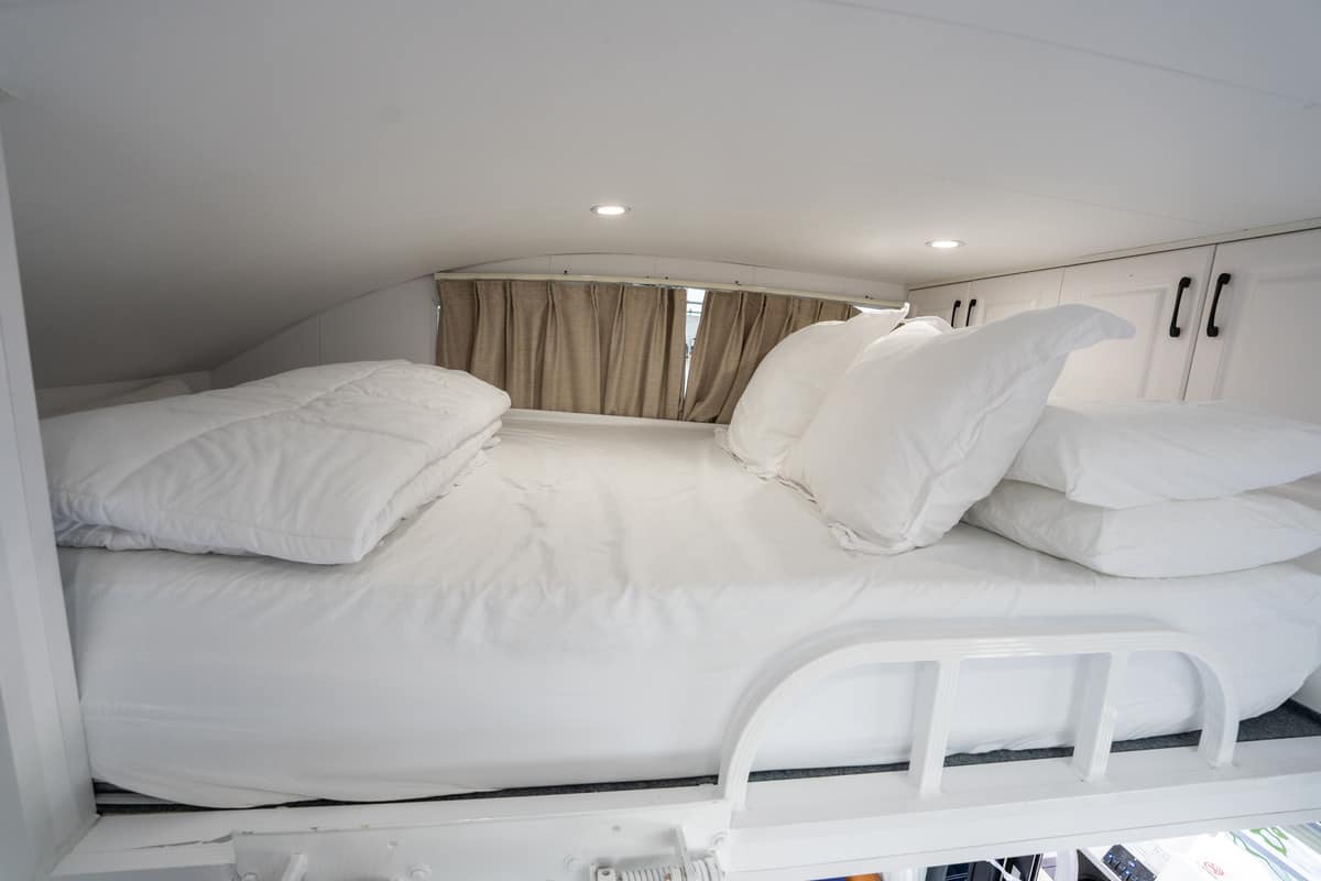 Compact sleeping area in a camper with white bedding and beige curtains.