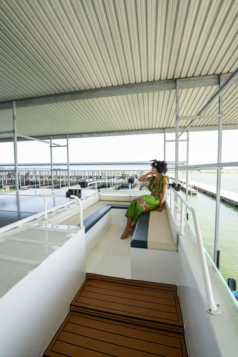 Person sitting on a boat deck with green water below, under a corrugated metal roof.