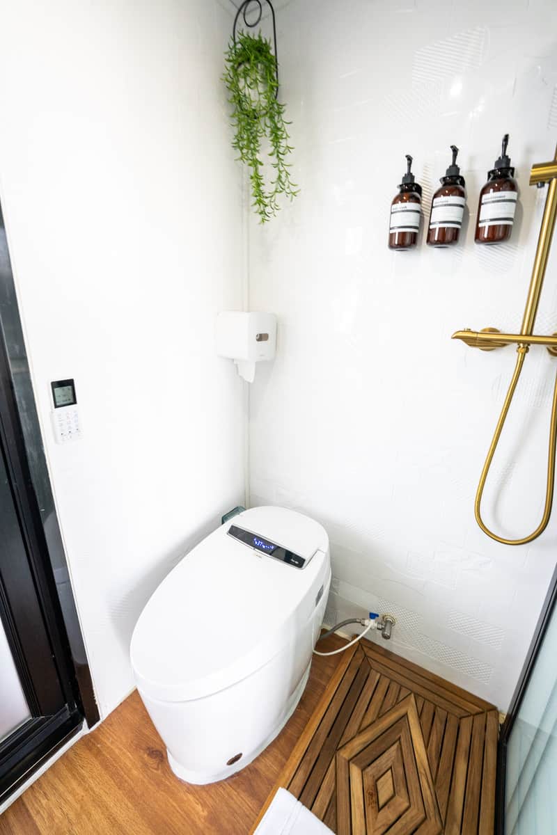 Modern toilet with electronic bidet, wooden floor, hanging plants, and wall-mounted soap bottles.