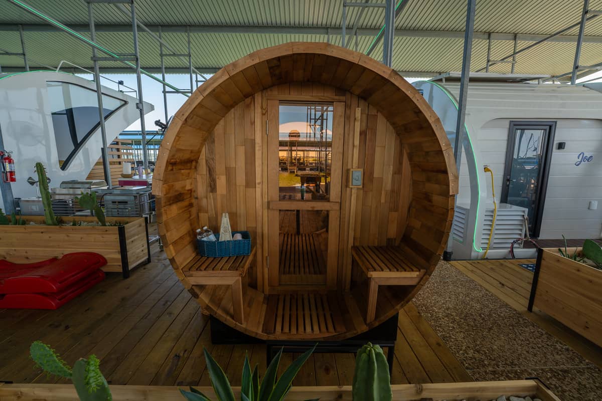 A round wooden cabin with a glass door, set against an indoor backdrop with plants and a boat.