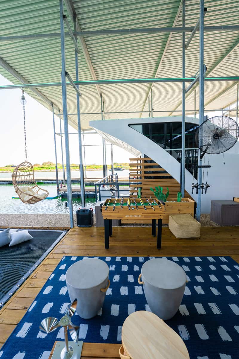 Modern outdoor lounge area with a hanging chair, foosball table, and waterfront view.