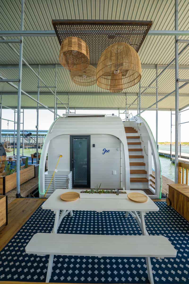 Modern pod-like structure with a staircase under a sheltered patio with wicker lamps and a white table.