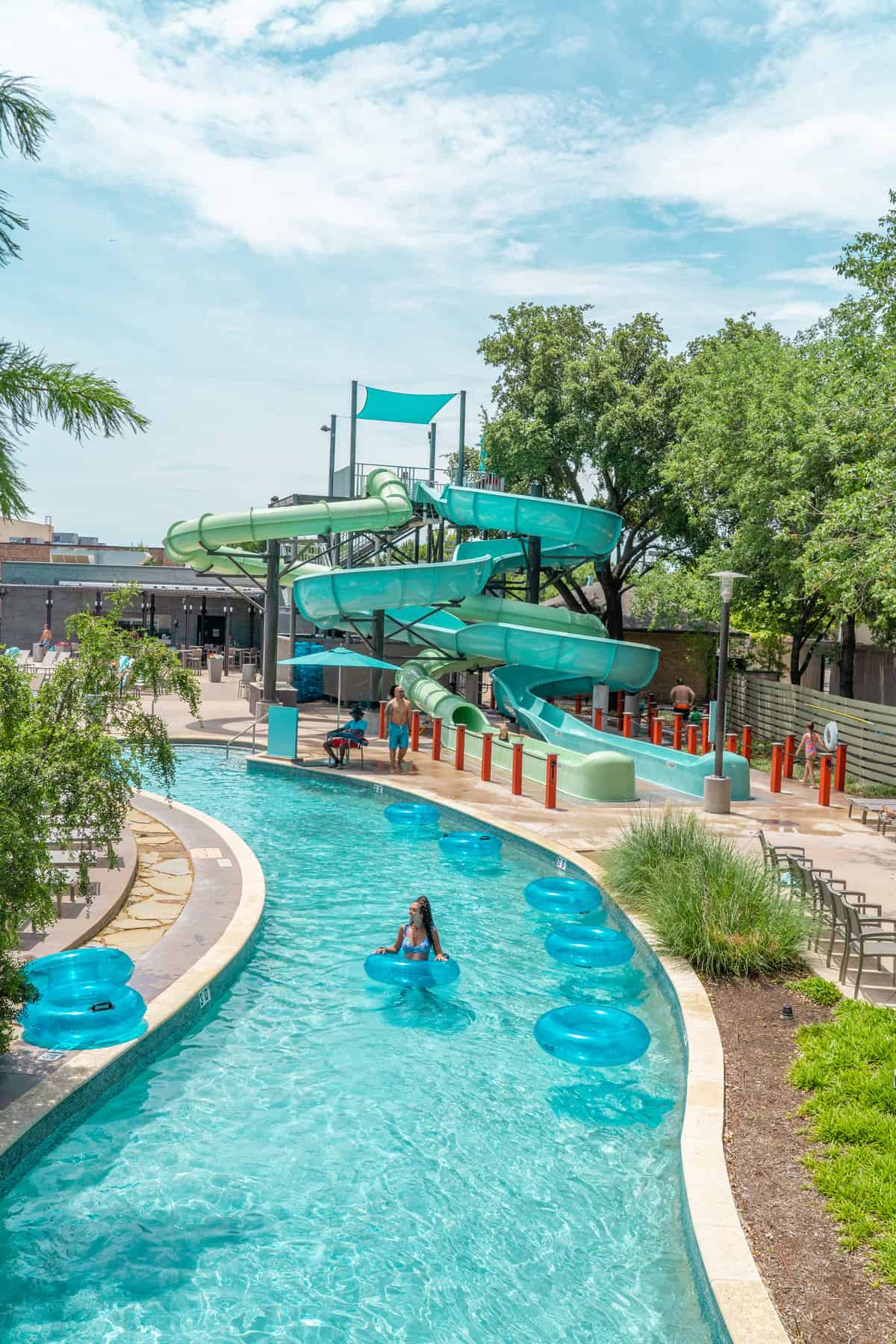 A water park with a green slide and people floating in a lazy river.