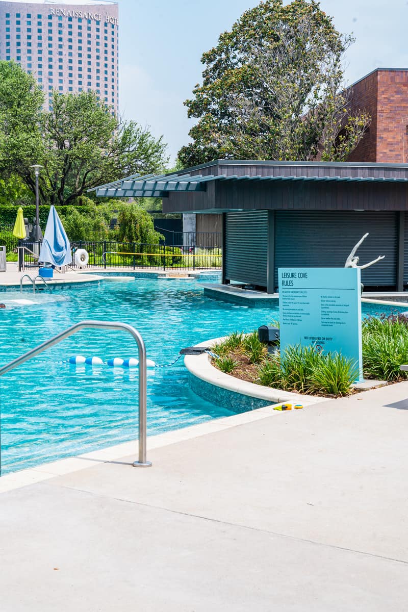 Outdoor pool area with a sign, handrail, and a hotel in the background.