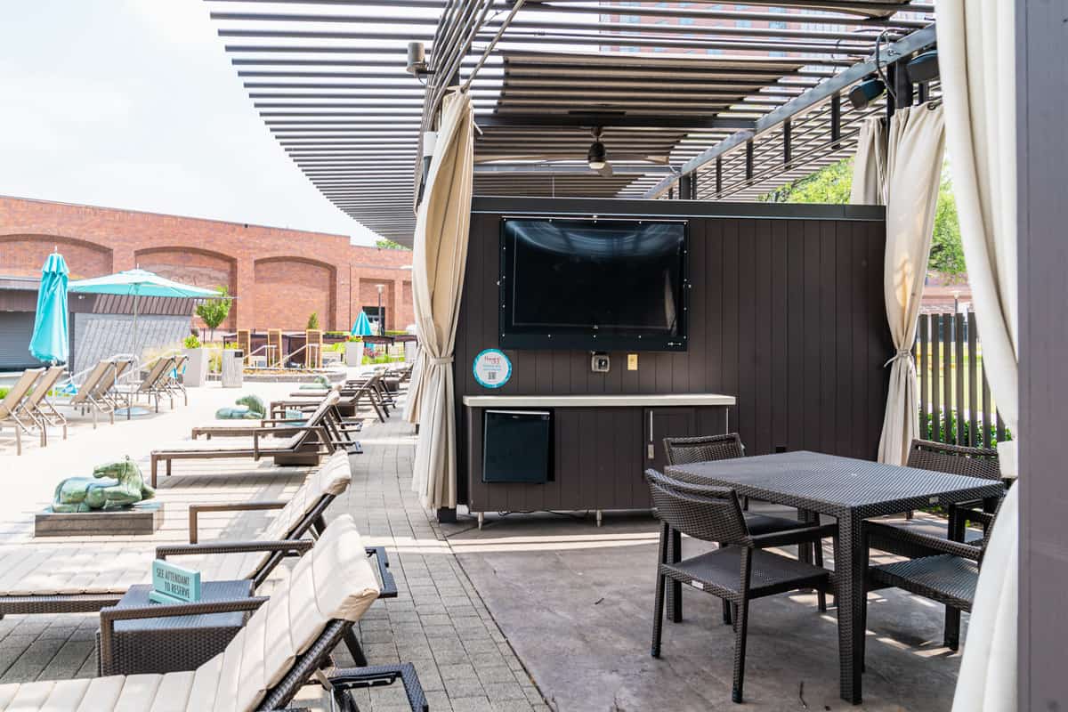 Outdoor patio area with television, seating, and poolside lounge chairs.