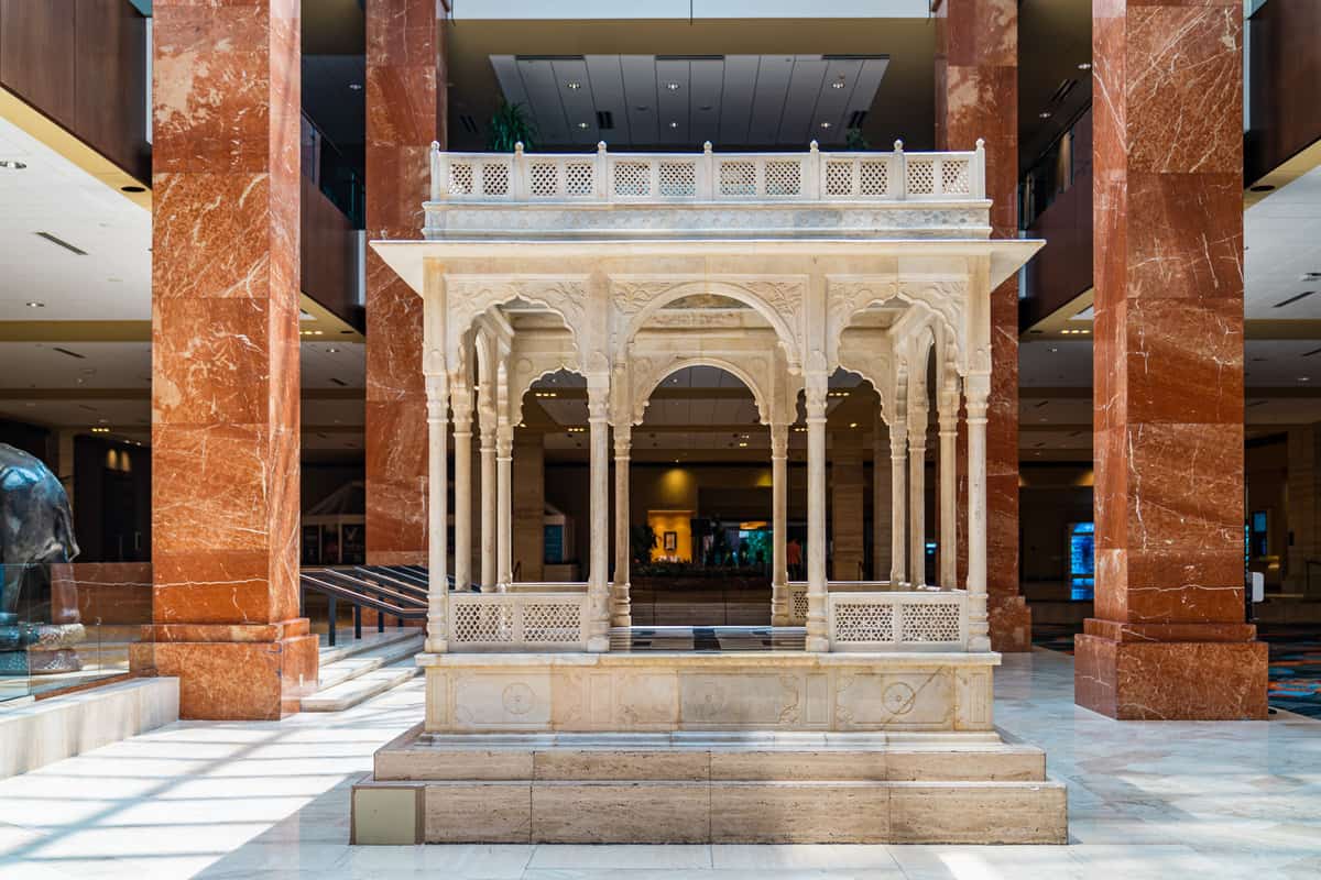 A marble gazebo with intricate carvings inside a lobby with polished stone columns.