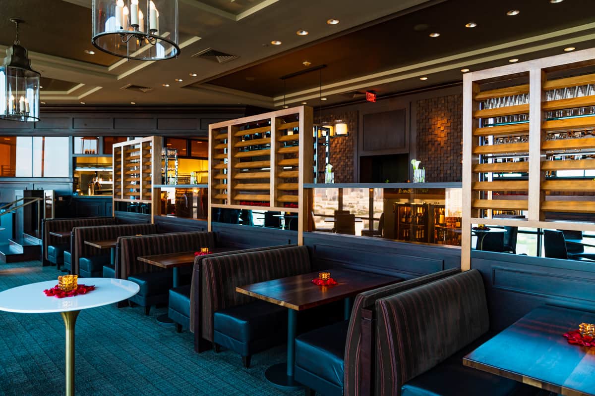 Modern restaurant interior with dark upholstered booths and wood wine racks.