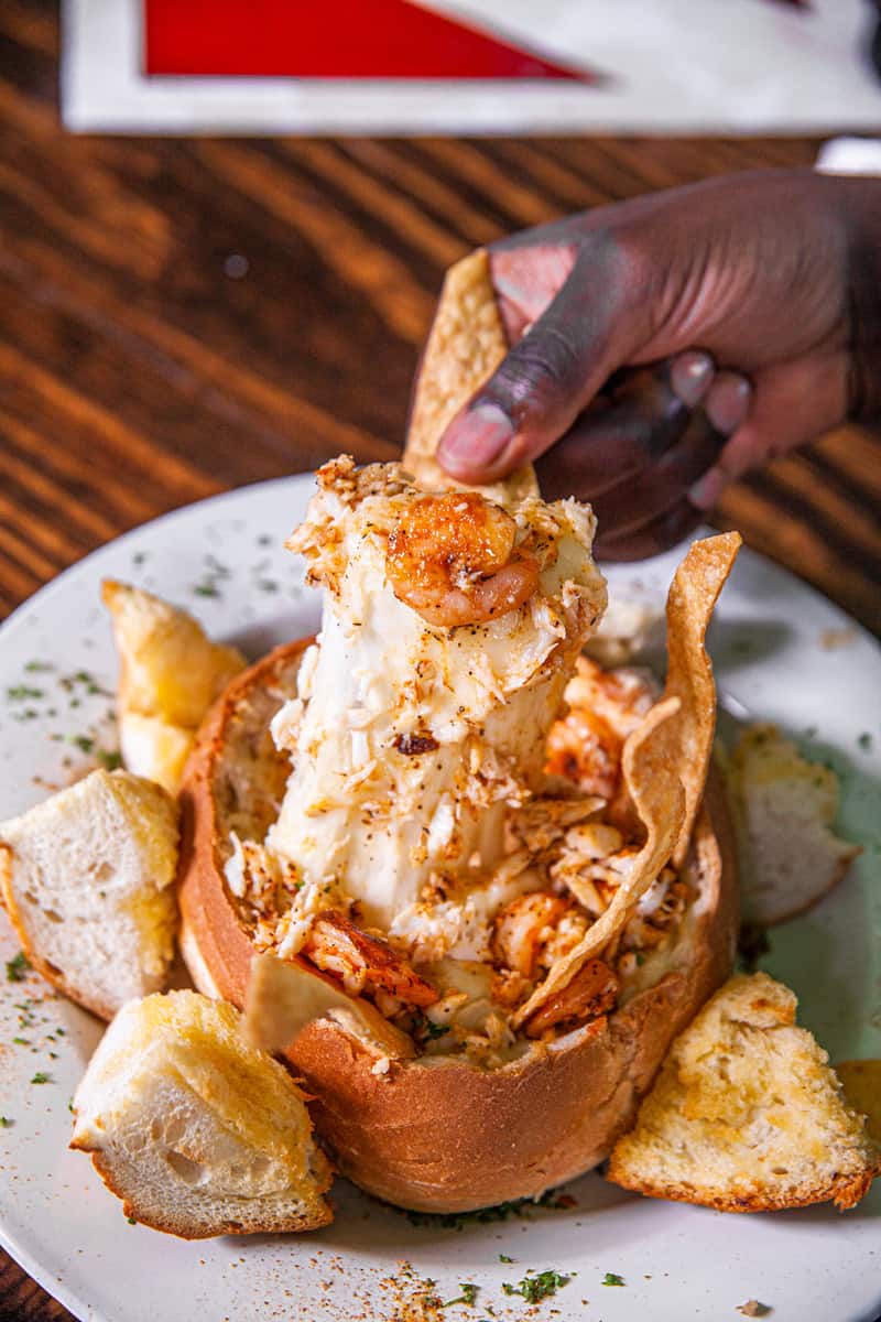a hand dipping a shrimp into a bread bowl