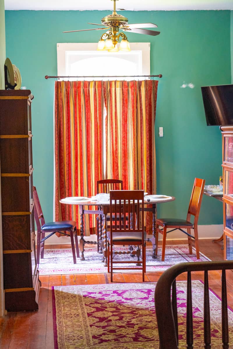 A wooden classic four seater dining table with Curtains and green walls 