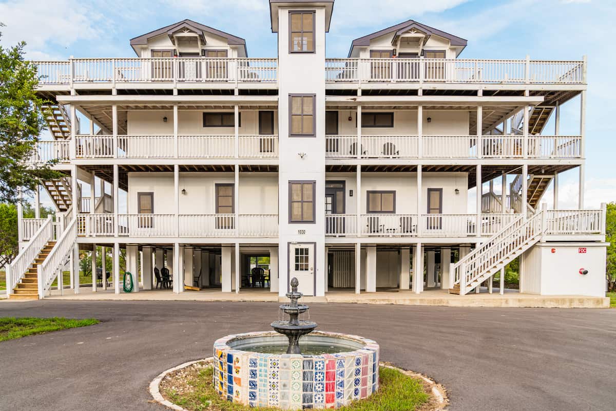 An off white, Victorian-style hotel building with a tile fountain in front