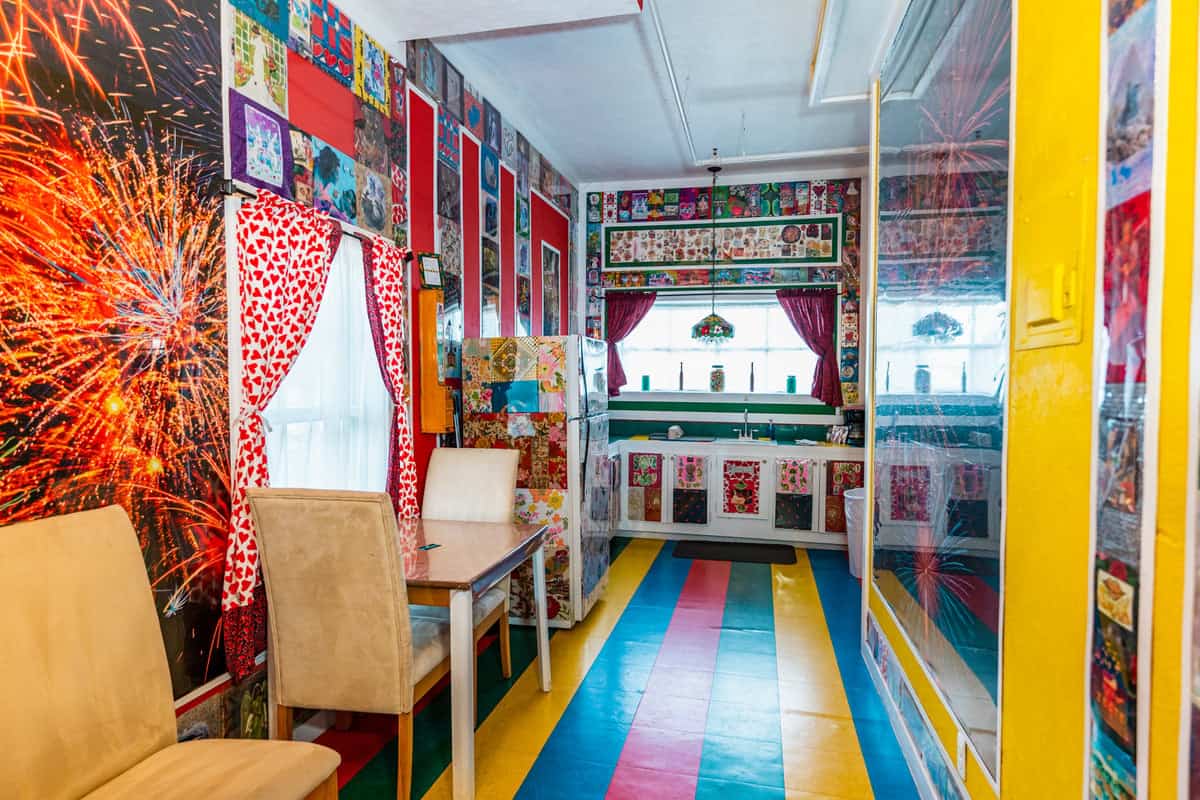 A kitchenette with a A stiped blue, yellow and red flooring and a wooden table and chairs and unique wall decors.