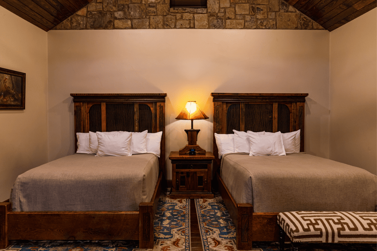 A lampshade in between two beds with wooden frames.