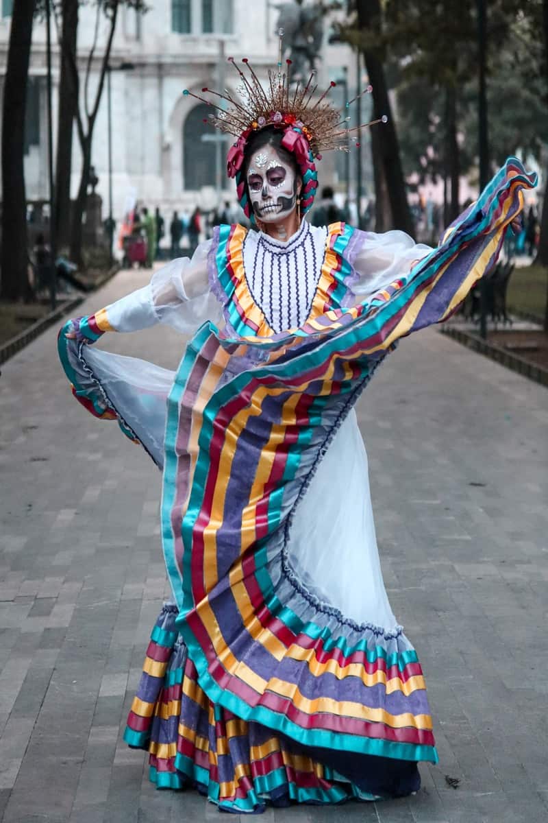 Woman in Catrina make-up and a folklorico dress with red, yellow, and blue frills on the skirt