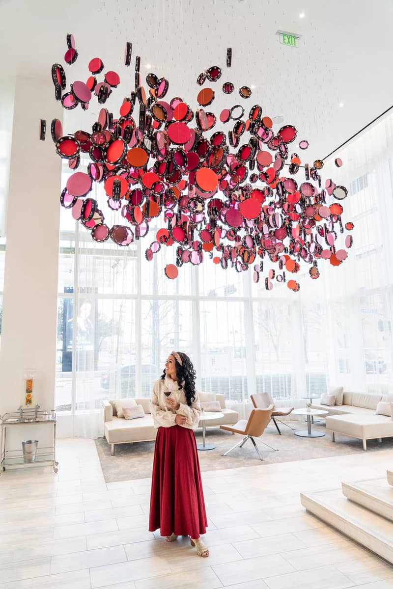 Woman standing under an art piece suspended from the ceiling with a wine glass in her hand