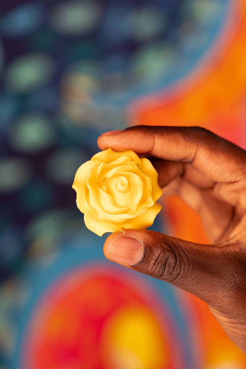 A hand holding a piece of chocolate that looks like a yellow rose