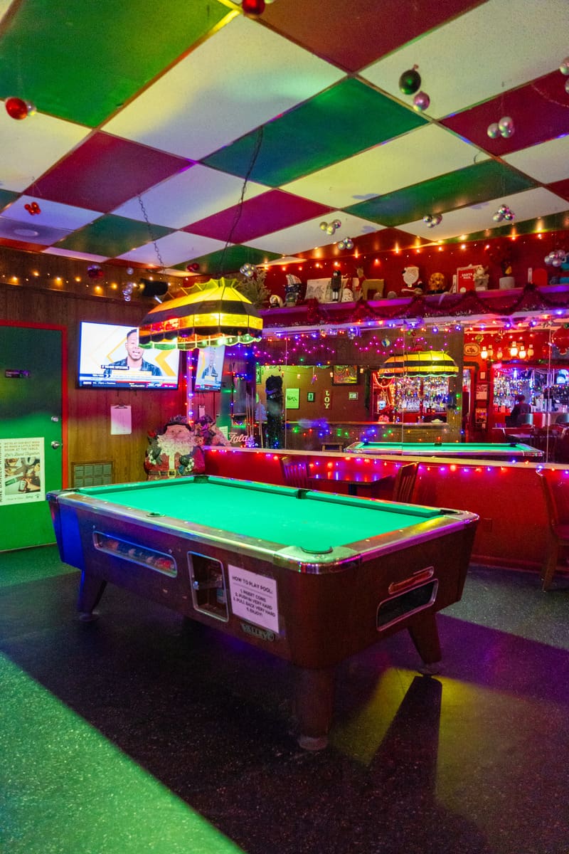 A pool table in a bar with a vibrant checkered ceiling in red and green 


