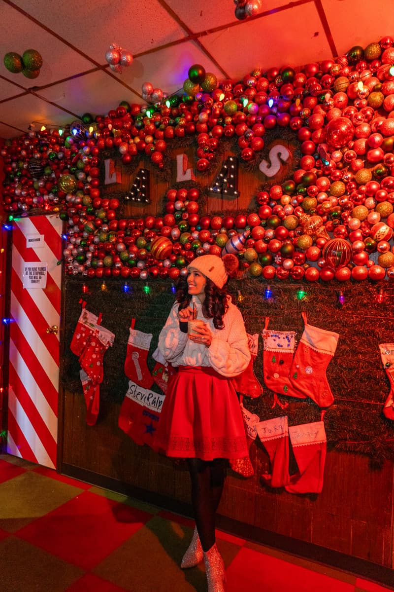 A woman in a red skirt  posing by a Christmas wall decor, radiating holiday cheer and elegance.