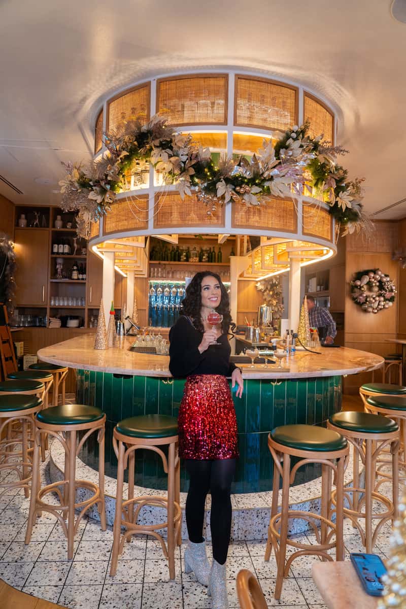 A stylish lady in a shiny red sequin skirt posing confidently in front of a vibrant bar.