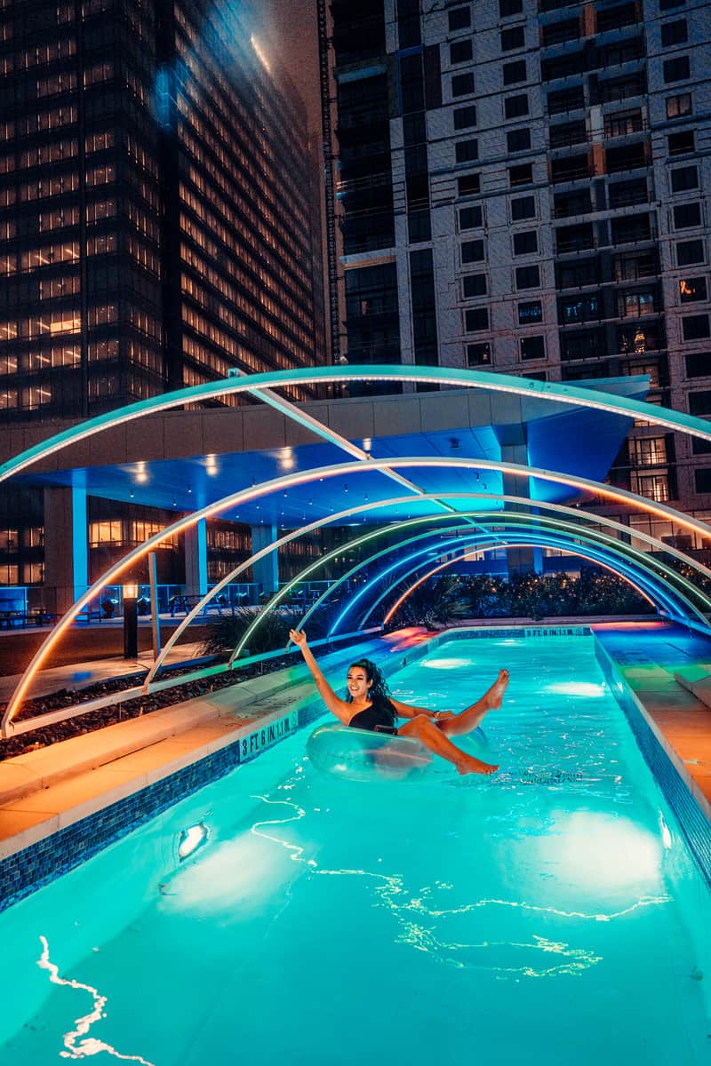 A woman enjoying a night swim on a pool with colorful lights.