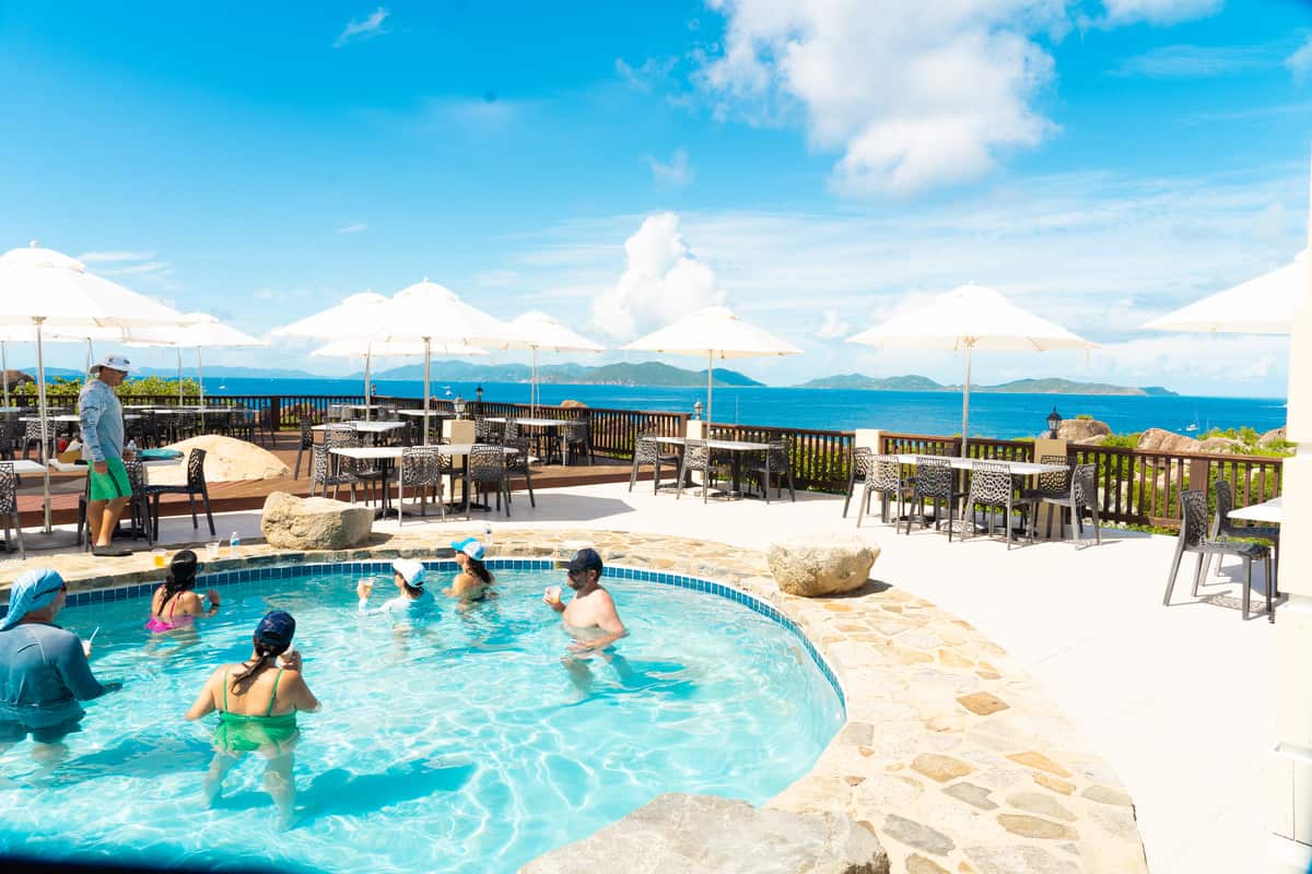 a group of people in a pool with umbrellas and chairs