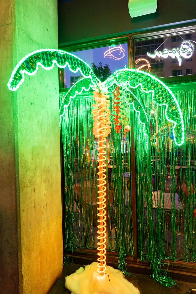 A human size palm tree indoor decoration adorned with twinkling lights, creating a magical and festive ambiance.