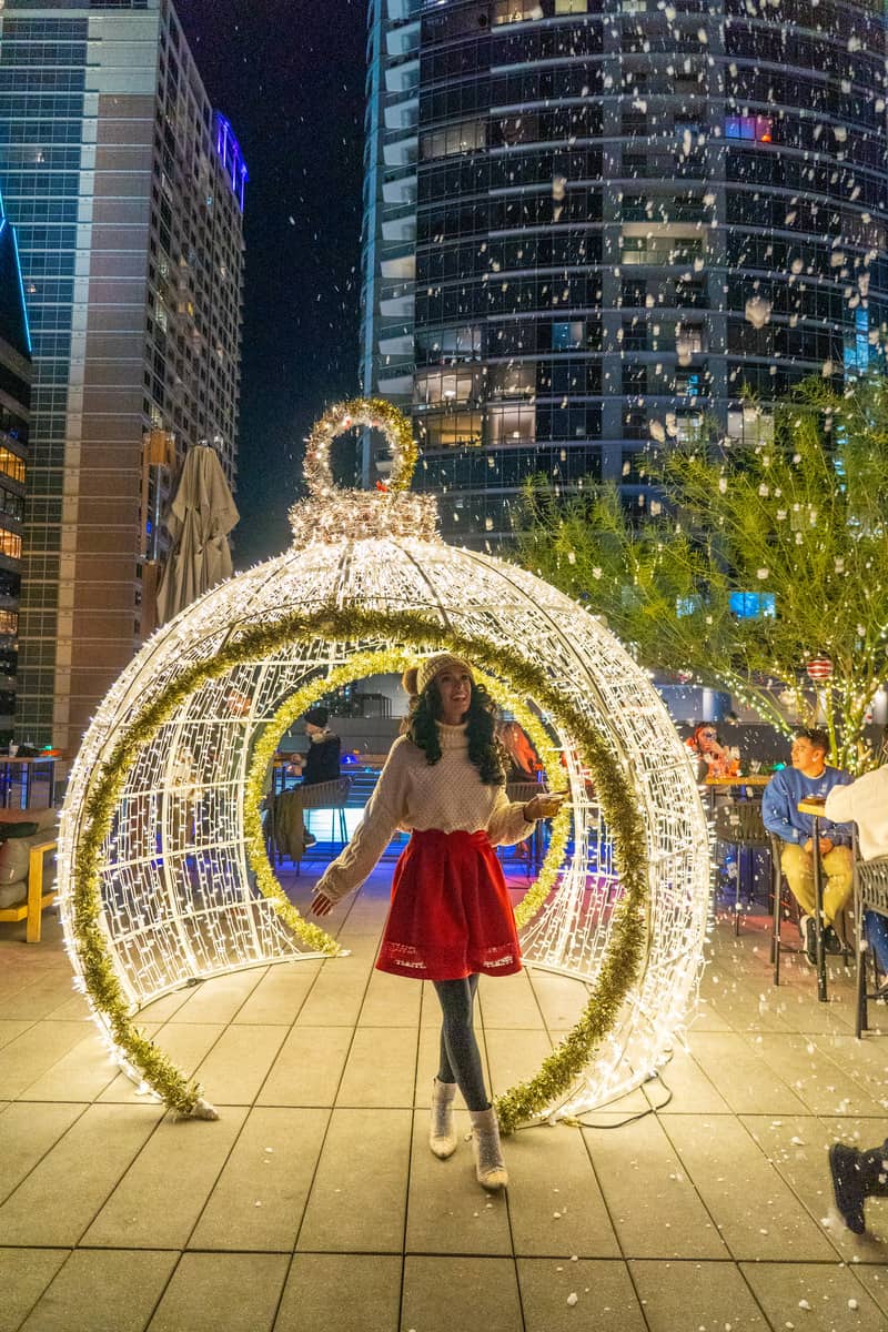 A woman in a red dress poses under a beautifully lit Christmas walkway 