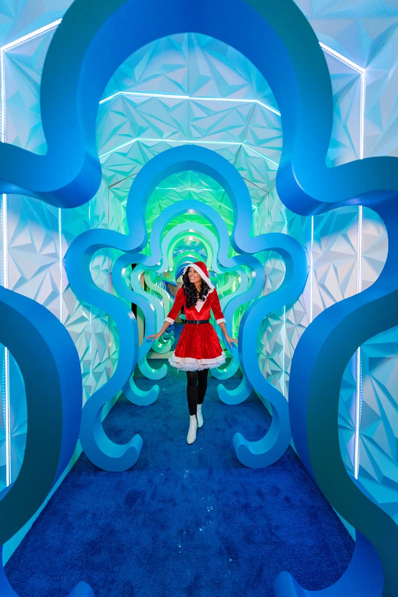 A woman in a Mrs. Santa dress gracefully strolls through a tunnel of giant ginger bread