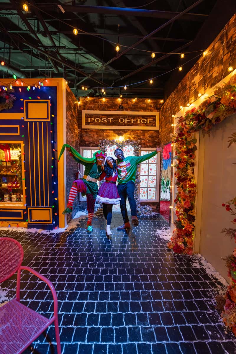 Three people enjoying a pose inside a festive room filled with colorful Christmas decorations.