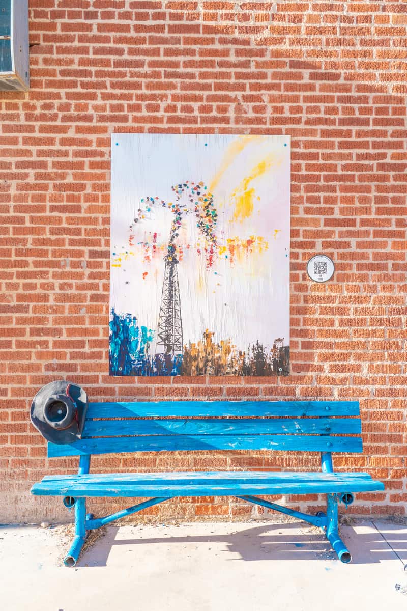 Colorful portrait painting hanging on a brick wall over a blue wooden bench