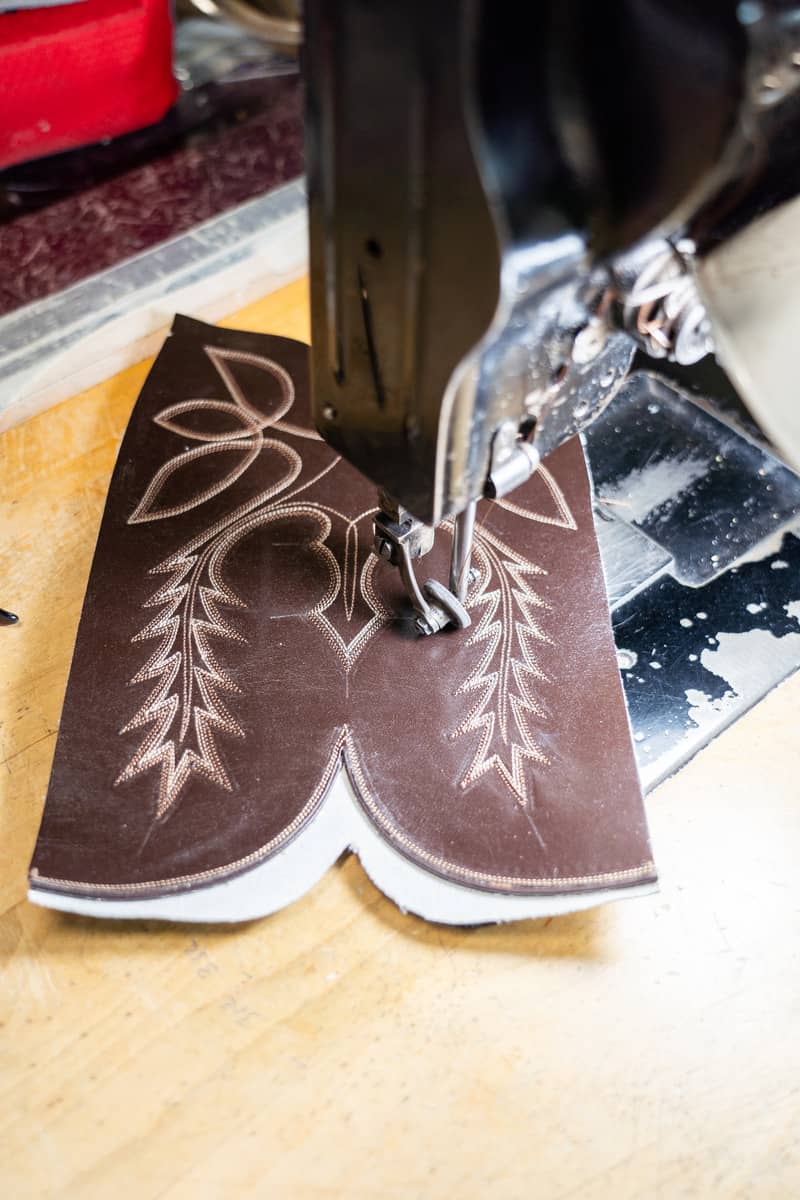 Sewing machine stitching a pattern onto a piece of brown leather for a pair of boots