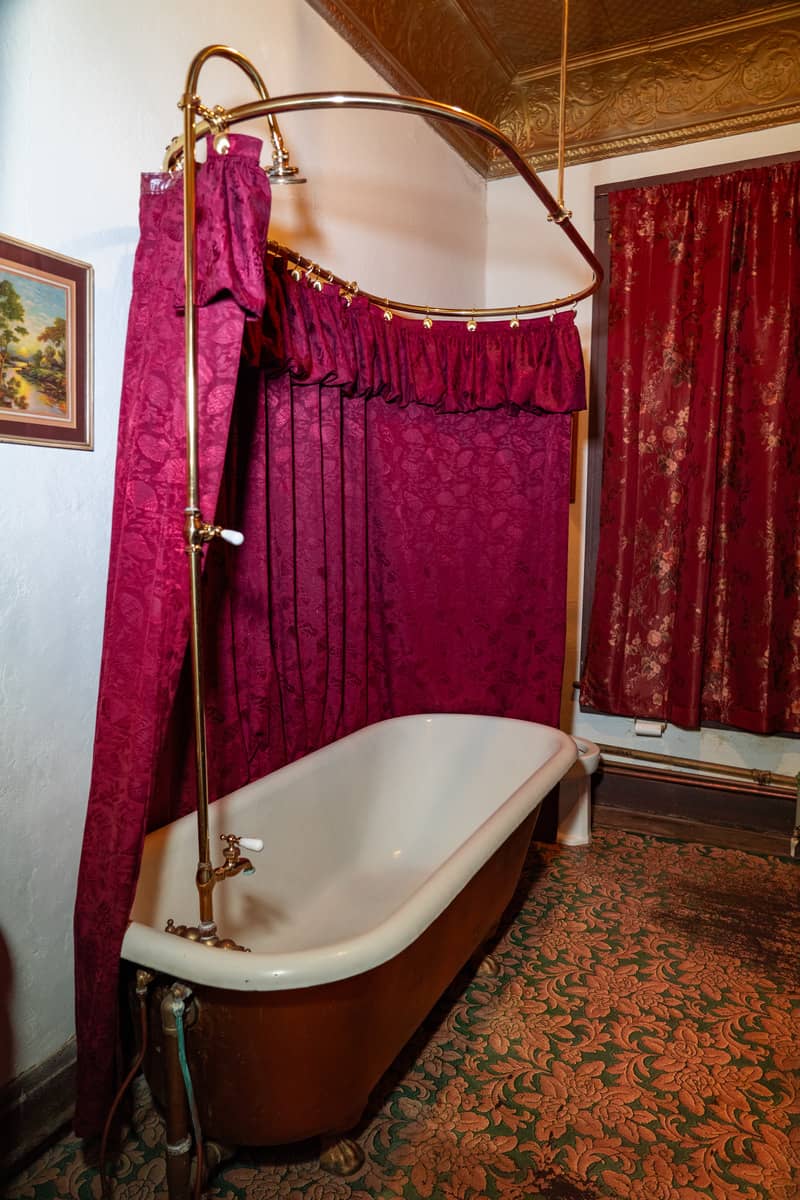 A soaking tub with a red curtain hanging from the ceiling between the tub and the wall