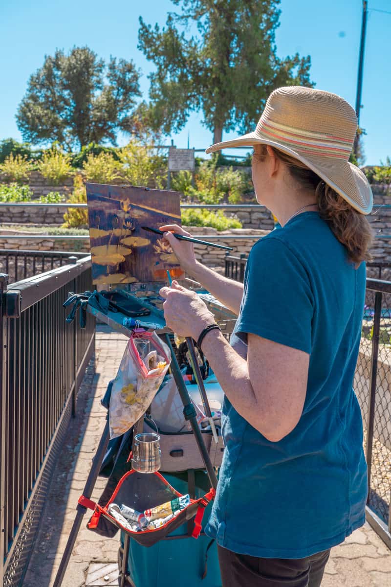 A woman in a sun hat painting her surroundings in the garden