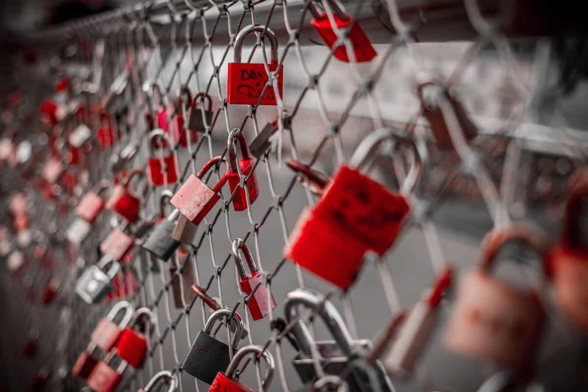 Several red locks on a wire metal bridge with writing on them in black marker