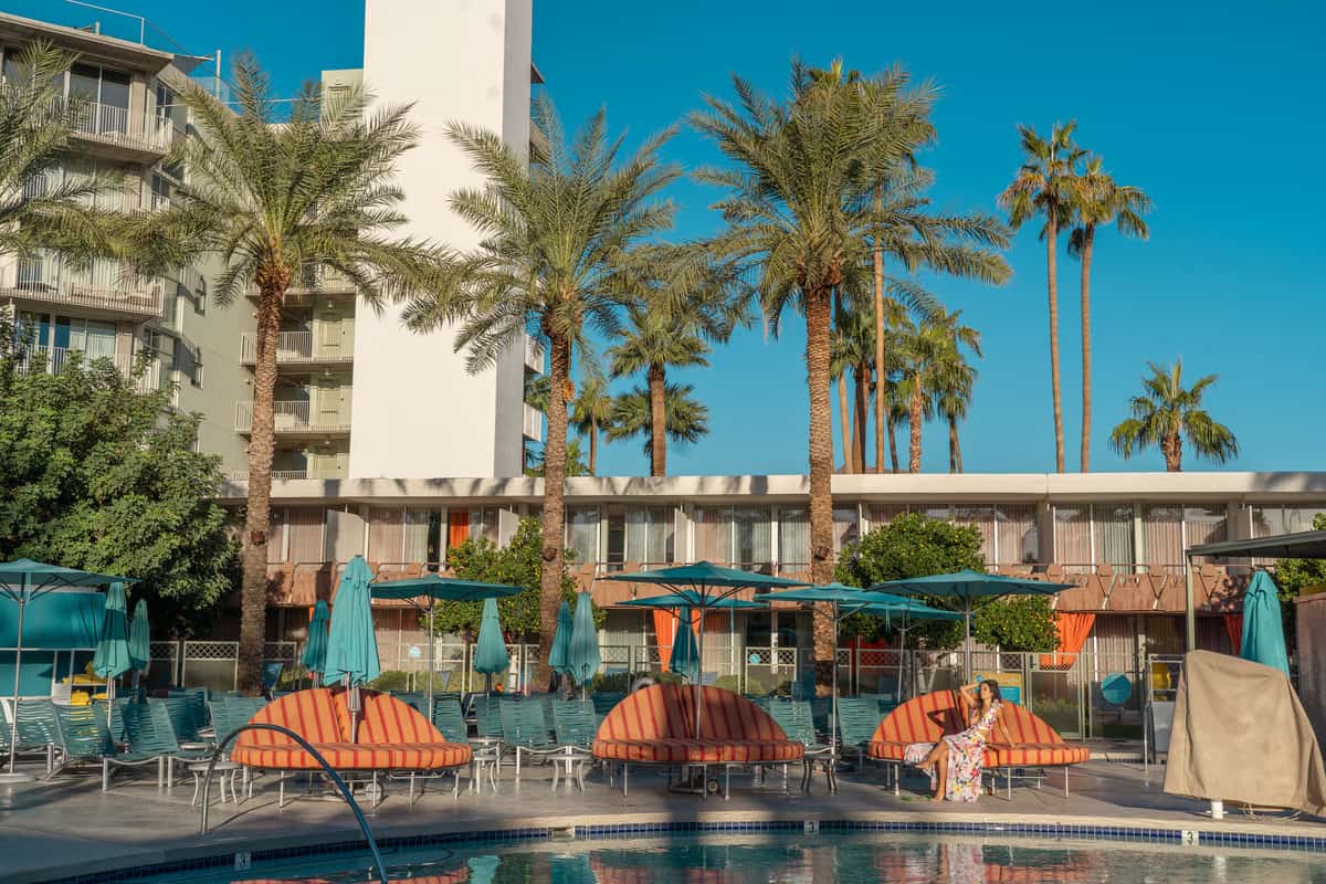 Pool with orange furniture and tall palm trees around it. You can see the main part of the hotel behind it.