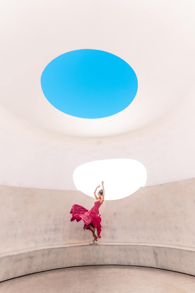 A woman in a red dress spinning in a bright, white room with a circular skylight on the ceiling