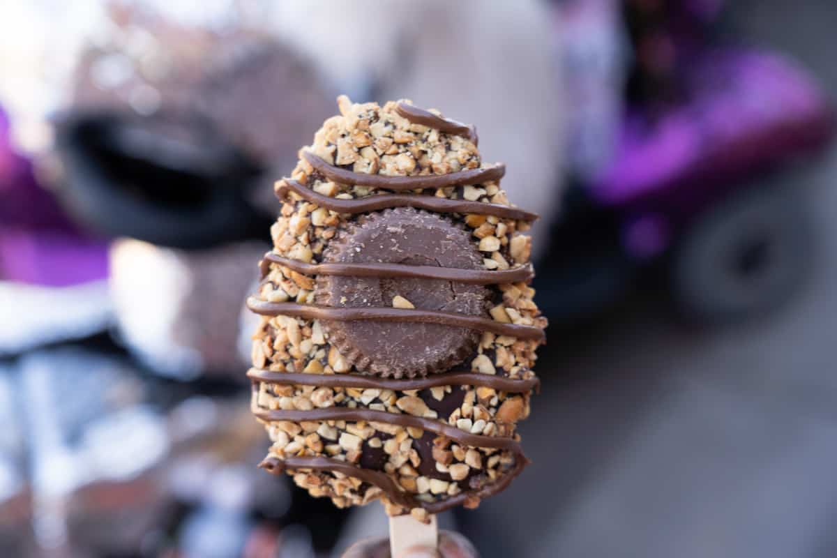 Hand-dipped ice cream bar covered in chocolate, chopped nuts, a Reese's cup, and chocolate drizzle
