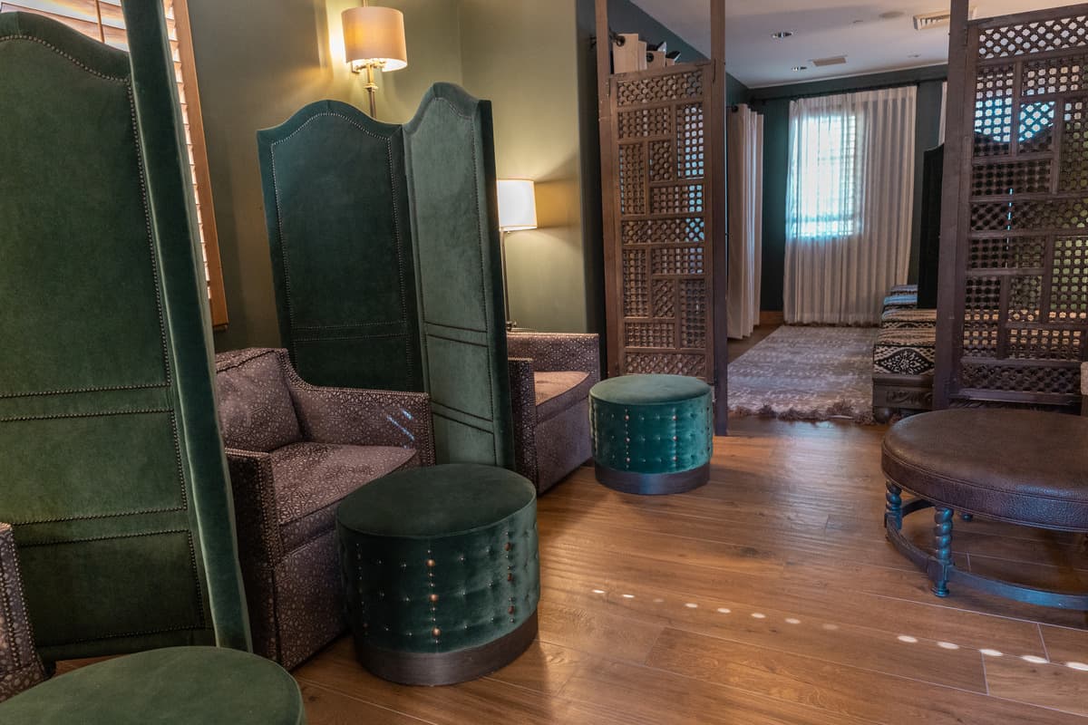 A hotel spa with purple armchairs and velvet green footstools separated by velvet green dividers