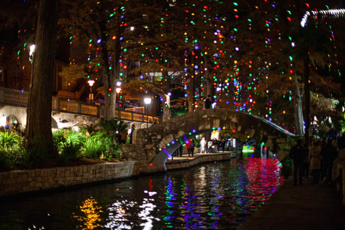 A riverside walkway illuminated by colorful hanging lights at night