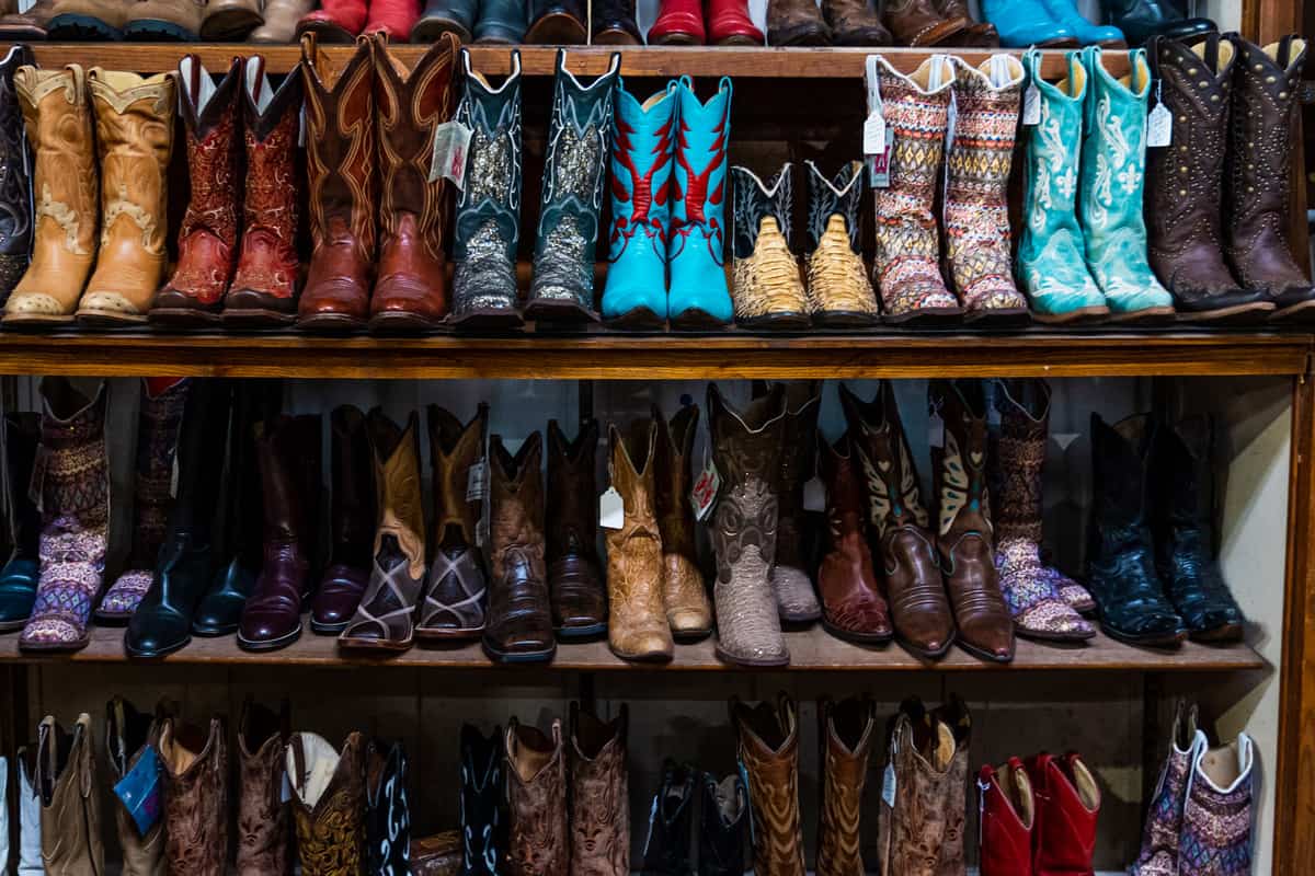 Three shelves filled with pairs of different colored and patterned cowboy boots.