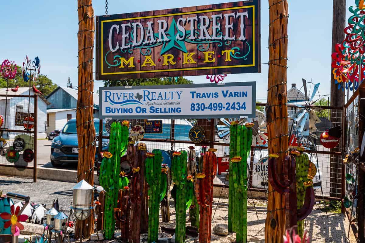Sign out front that says Cedar Street Market with yard decorations on display in front of it