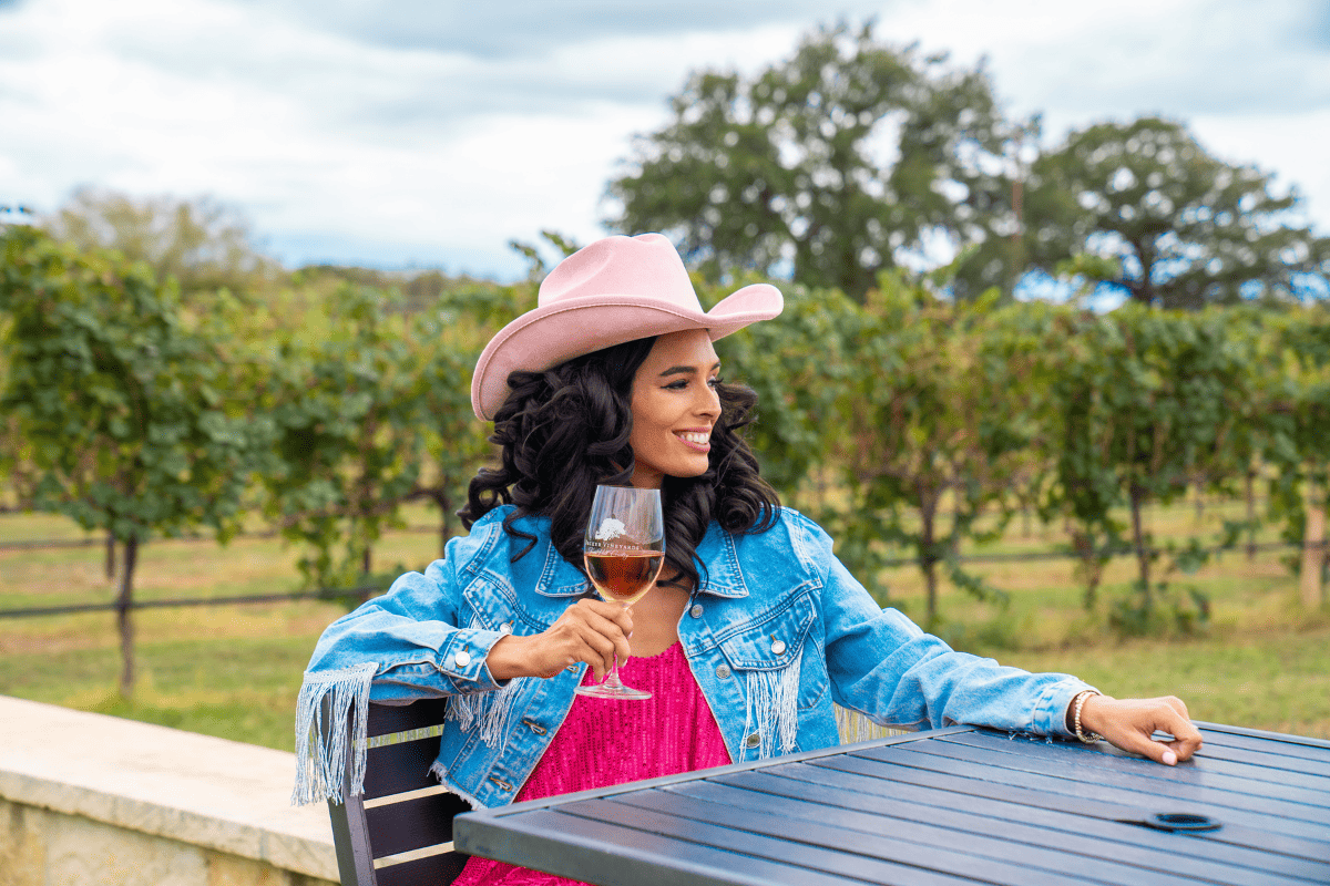 A woman in a cowboy hat gracefully holds a glass of wine
