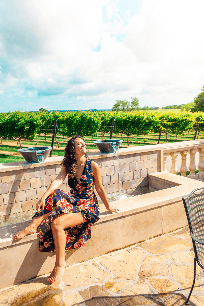 A woman enjoying a peaceful moment, sitting on a stone wall, on a vineyard.